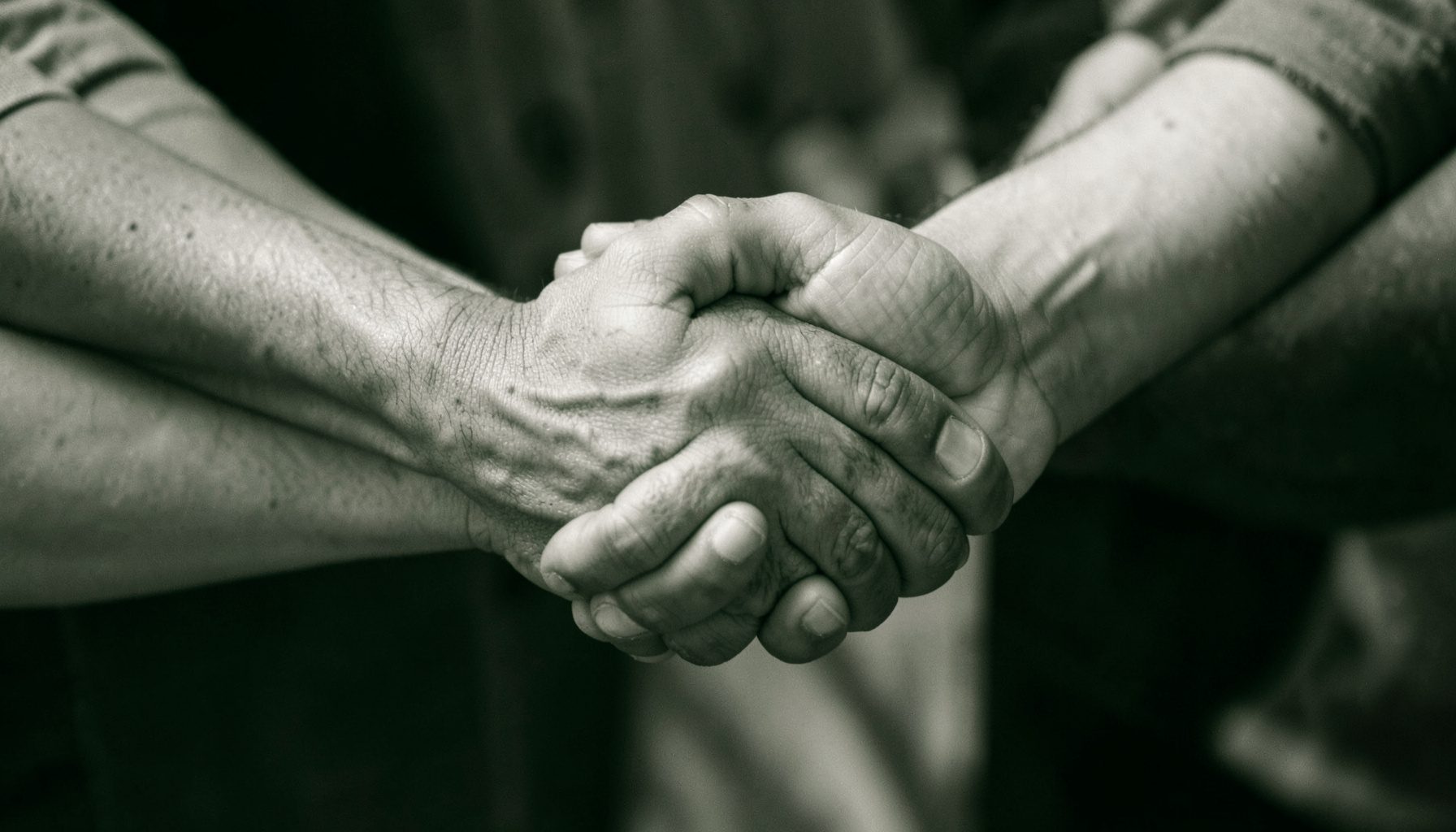 Fotografia in duotone bianco e nero di mani che si stringono in segno di solidarietà, toni caldi e avvolgenti